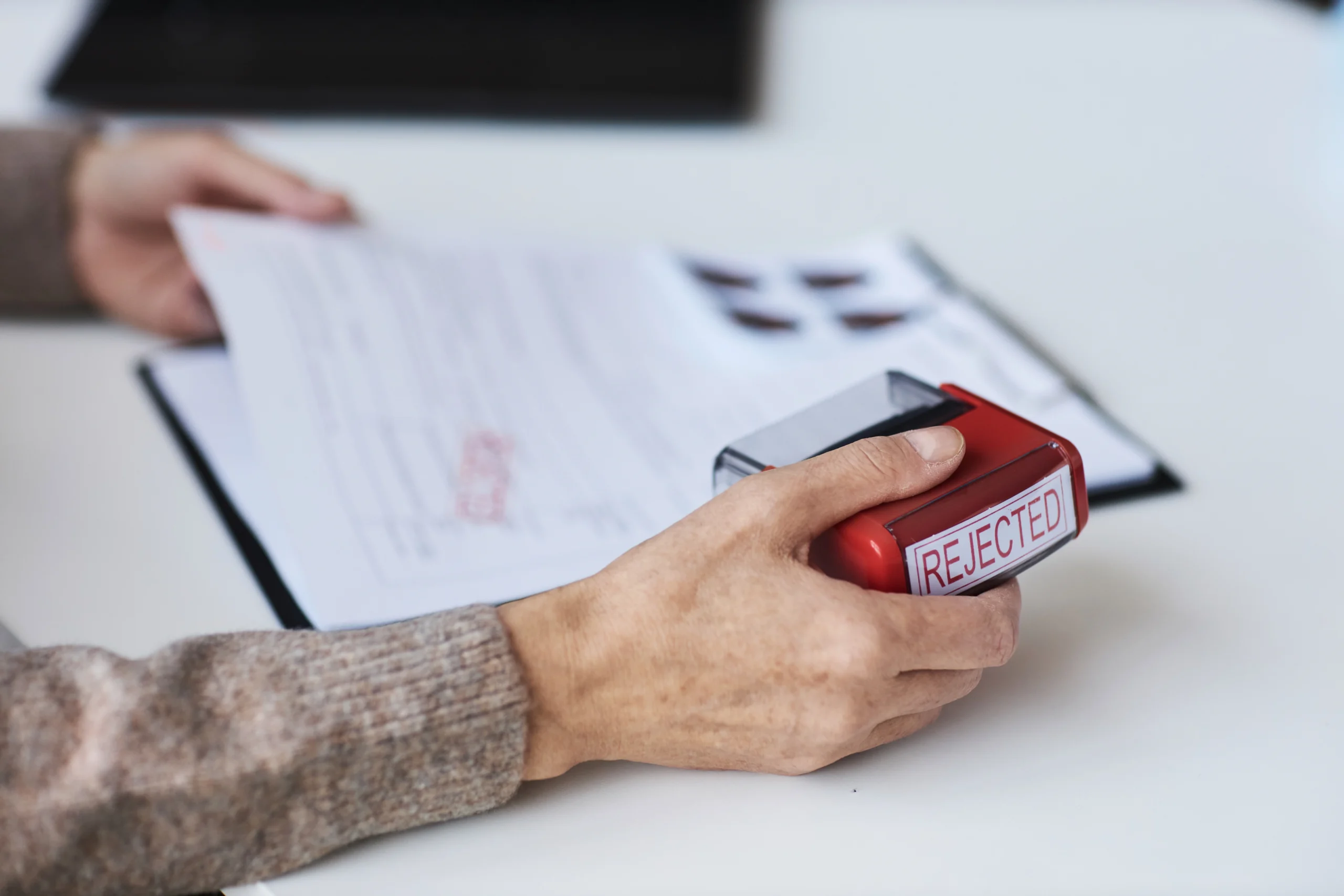 Manos sosteniendo un documento de seguro de vida con un sello rojo de "Rechazado"
